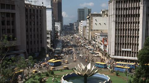 Dhaka, der Hauptstadt Bangladesh. Im Vordergrund verläuft die Straße um eine kreisförmige Grünanlage mit Brunnen. Aufnahme vom Mai 1990.