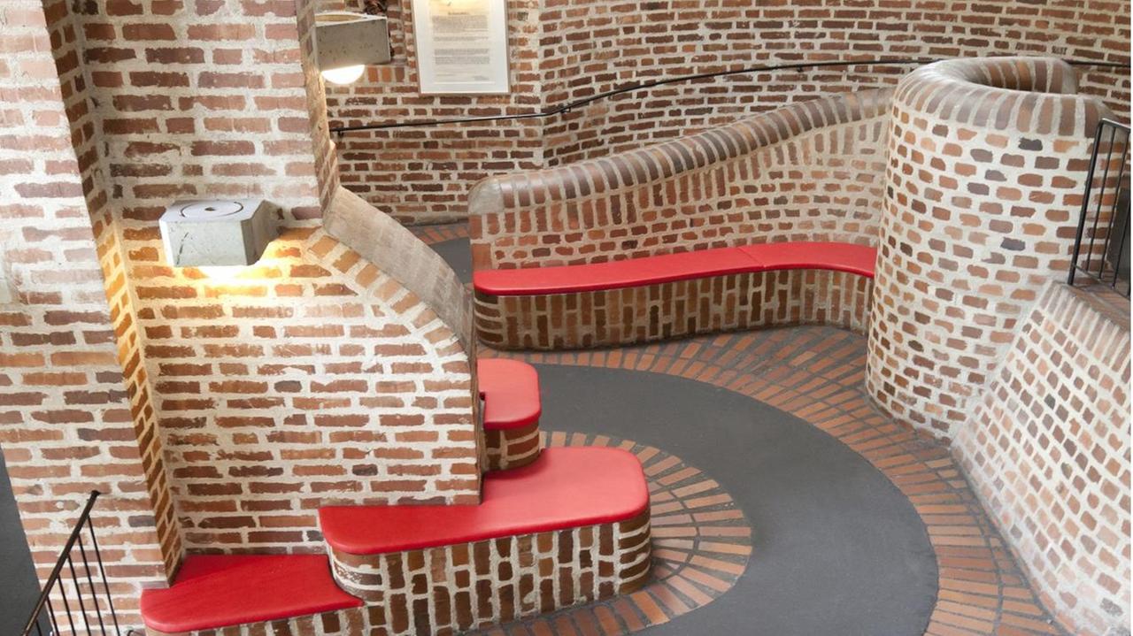 Das alte Gebäude des Altenzentrums St. Hildegard ist aus Backstein: Die Wege aus schwarzem Asphalt schlängeln sich durch Sitzgelegenheiten, auch die Sitzbänke sind aus Backstein gebaut. Das alte Gebäude des Altenzentrums St. Hildegard ist aus Backstein: Die Wege aus schwarzem Asphalt schlängeln sich durch Sitzgelegenheiten, auch die Sitzbänke sind aus Backstein gebaut.