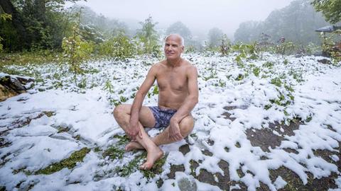 Ein älterer Mann sitzt nur in Unterhose auf einer schneebedeckten Wiese.