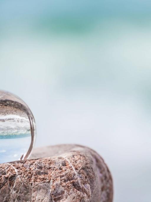 In einer Glaskugel spiegelt sich die Adriaküste, die im Hintergrund nur unscharf zu sehen ist.