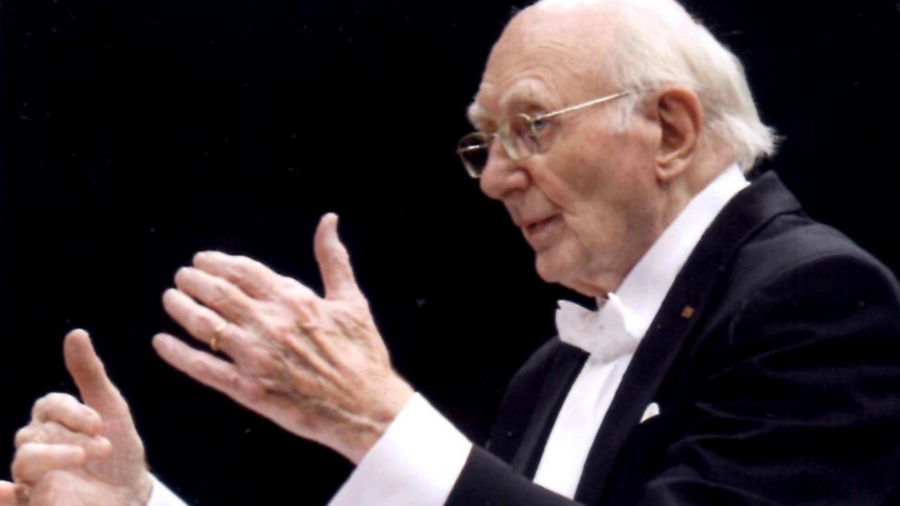 Ein Mann mit weißen Haaren in einem Frack dirigiert ein Orchester. Ein Mann mit weißen Haaren in einem Frack dirigiert ein Orchester.
