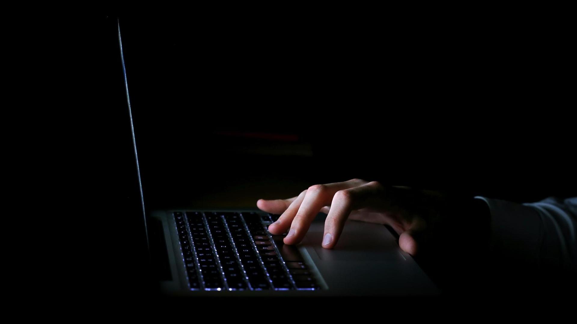 Eine Hand im Dunkeln über der beleuchteten Tastatur eines Laptops.