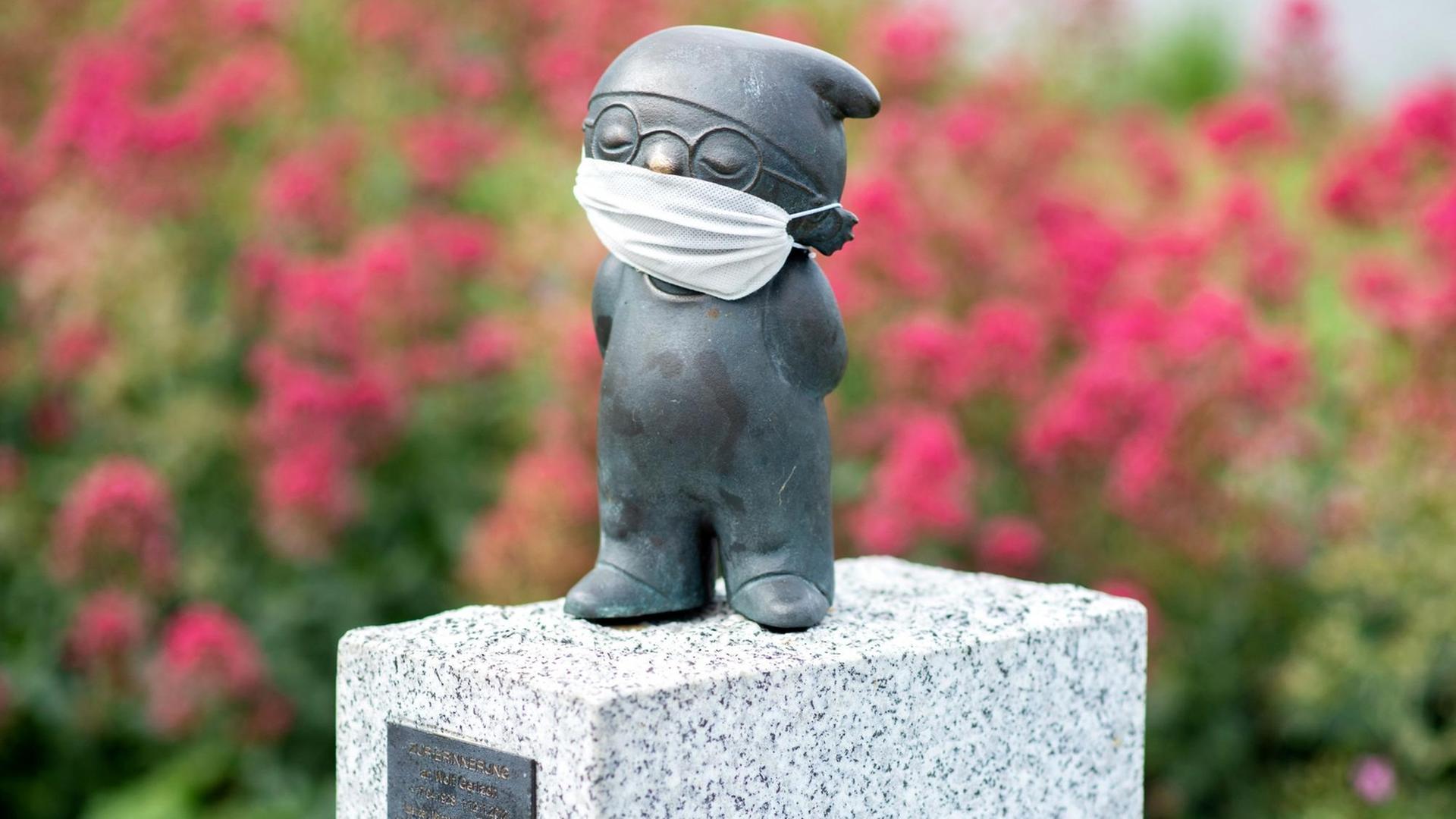 Eine Bronzefigur von einem ZDF-Mainzelmännchen, bekleidet mit einem Mund-Nasen-Schutz Eine Bronzefigur von einem ZDF-Mainzelmännchen, bekleidet mit einem Mund-Nasen-Schutz