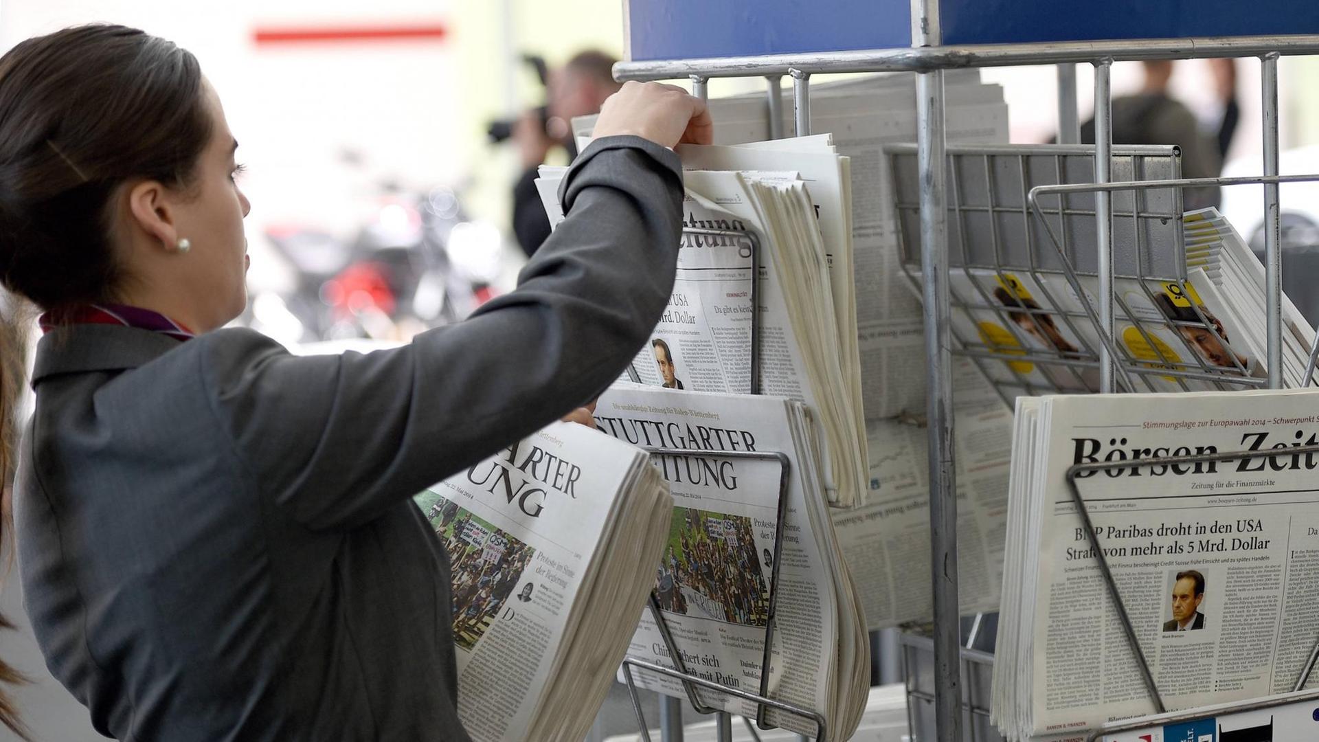 Eine Frau füllt einen Zeitungsständer auf.