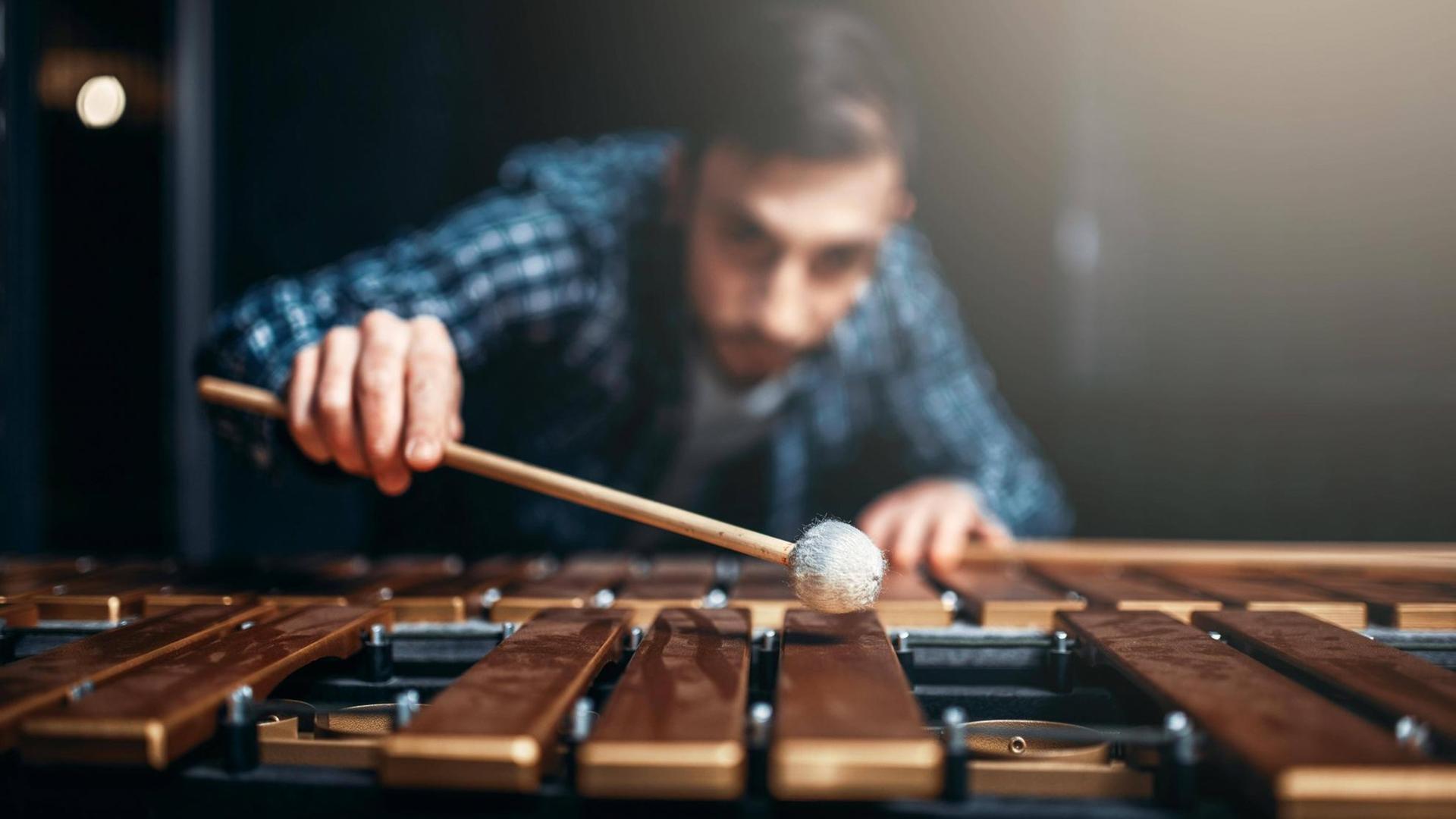 Ein Xylophon-Spieler beugt sich mit Schlägern über sein Instrument. Ein Xylophon-Spieler beugt sich mit Schlägern über sein Instrument.