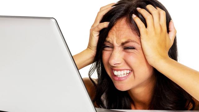 Eine junge Frau fasst sich verzweifelt an den Kopf, während sie vor ihrem Laptop sitzt