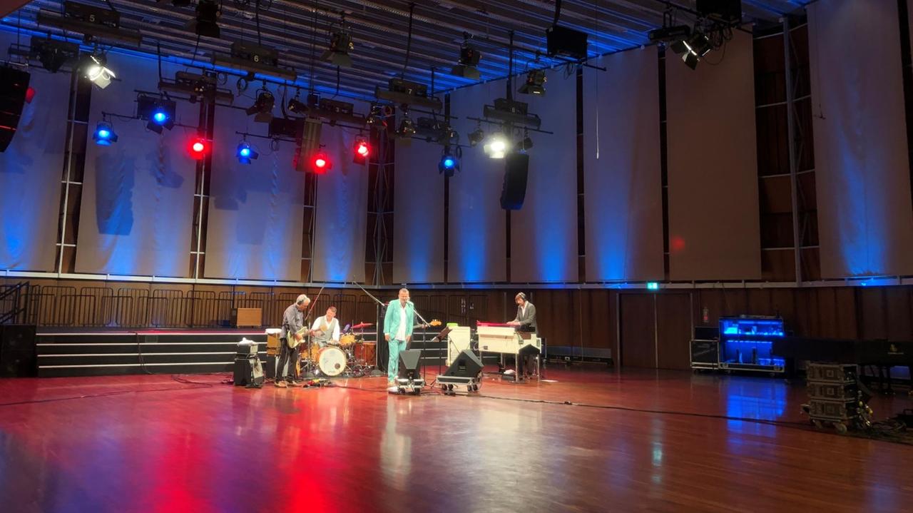 Fünf Musiker stehen mit ihren Instrumenten im 500 Quadratmeter großen Saal, der von bunten Scheinwerfern erleuchtet wird. Fünf Musiker stehen mit ihren Instrumenten im 500 Quadratmeter großen Saal, der von bunten Scheinwerfern erleuchtet wird.