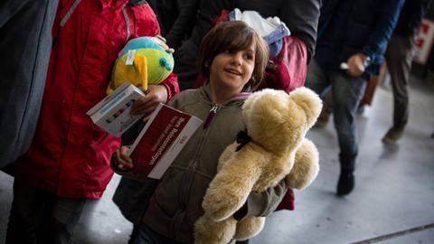 Flüchtlingskind mit einem Teddybär im Arm auf dem Bahnhof.