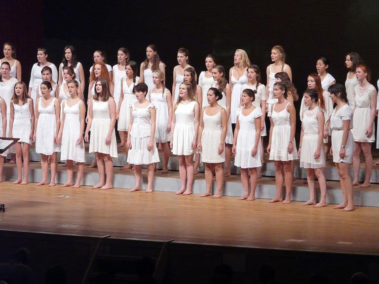 Der Chor steht mit weißen Kleidern und barfuß auf der Bühne.