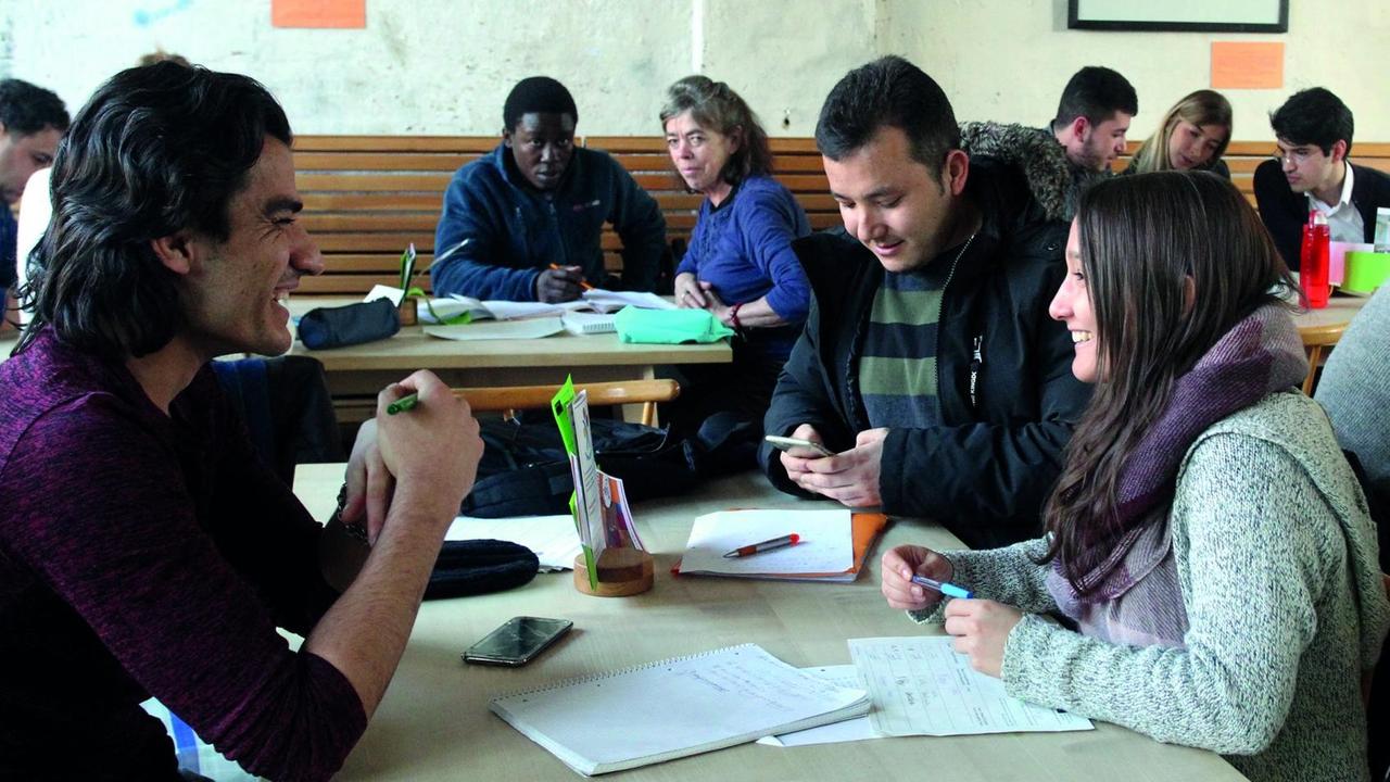 Menschen, die sich unterhalten und lachen, sitzen im Lerncafé "Tür an Tür" des gleichnamigen Vereins in Augsburg. Auf den Tischen liegen Unterlagen wie Hausaufgaben. Menschen, die sich unterhalten und lachen, sitzen im Lerncafé "Tür an Tür" des gleichnamigen Vereins in Augsburg. Auf den Tischen liegen Unterlagen wie Hausaufgaben.