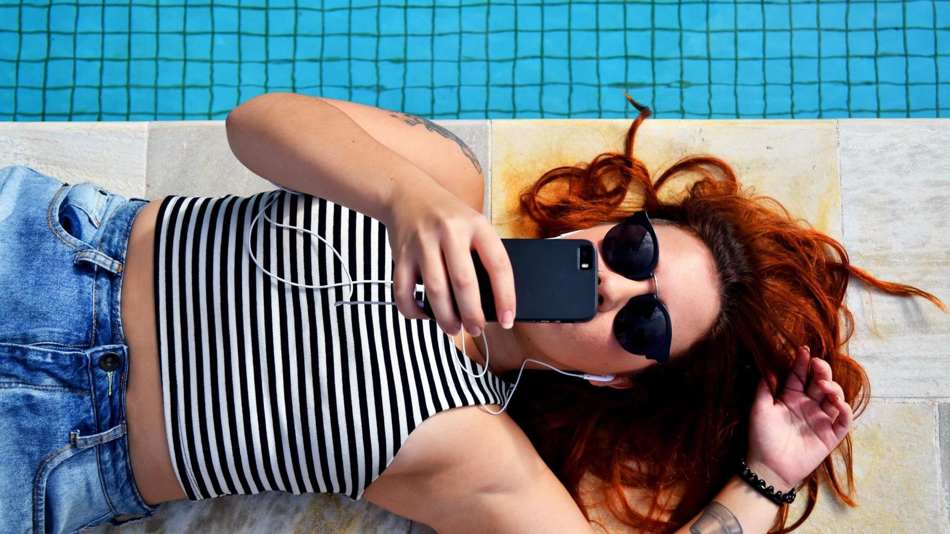 Eine junge Frau liegt am Rand eines Pools und kommunziert über ihr Handy. Eine junge Frau liegt am Rand eines Pools und kommunziert über ihr Handy.
