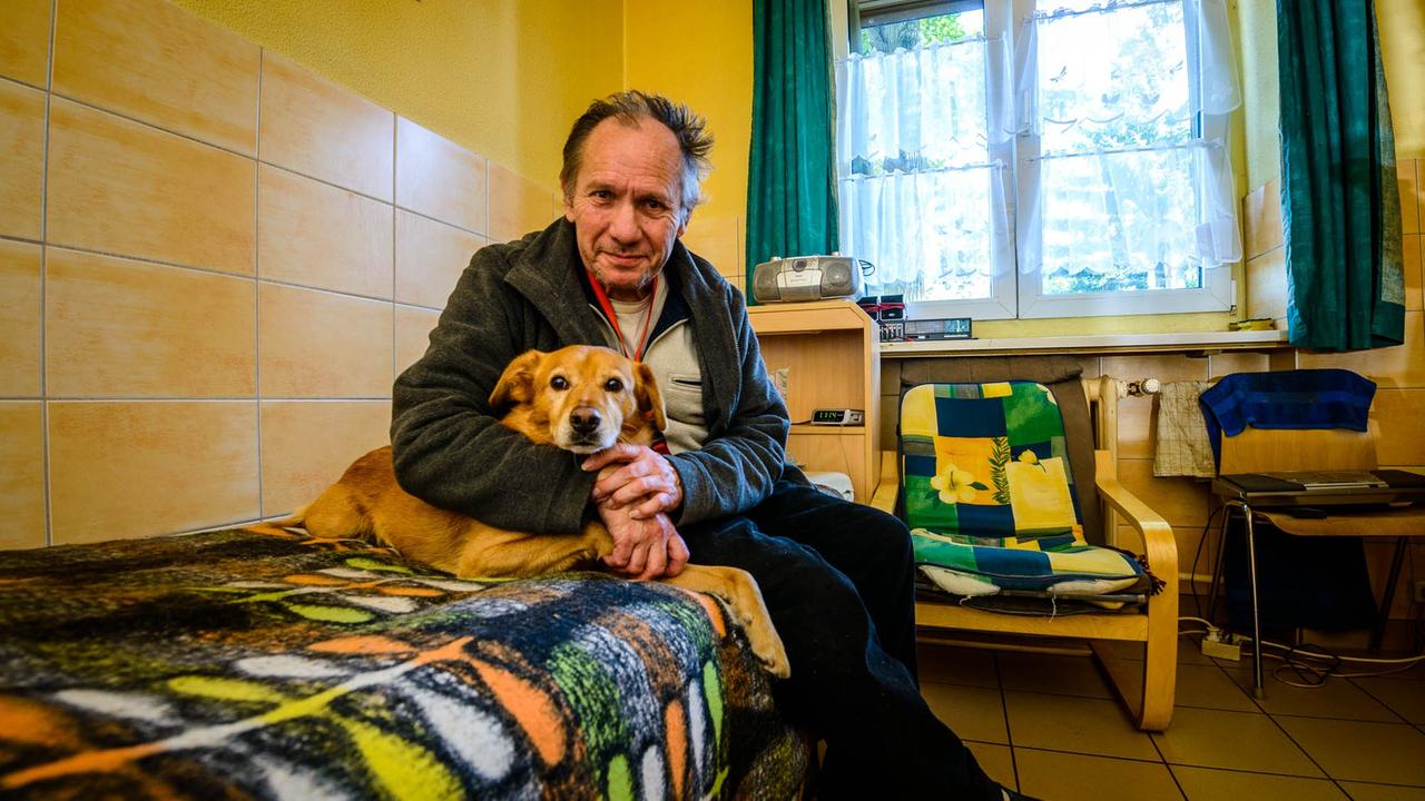 Ein ehemaliger Obdachlose sitzt zusammen mit einem Hund im Arm auf einem Bett in einem Zimmer des William-Booth-Haus der Heilsarmee in Berlin. Ein ehemaliger Obdachlose sitzt zusammen mit einem Hund im Arm auf einem Bett in einem Zimmer des William-Booth-Haus der Heilsarmee in Berlin.