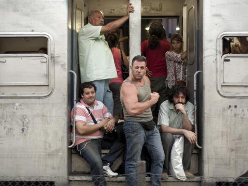 An einer Zugtür zeigt ein Mann seinen Bizeps.