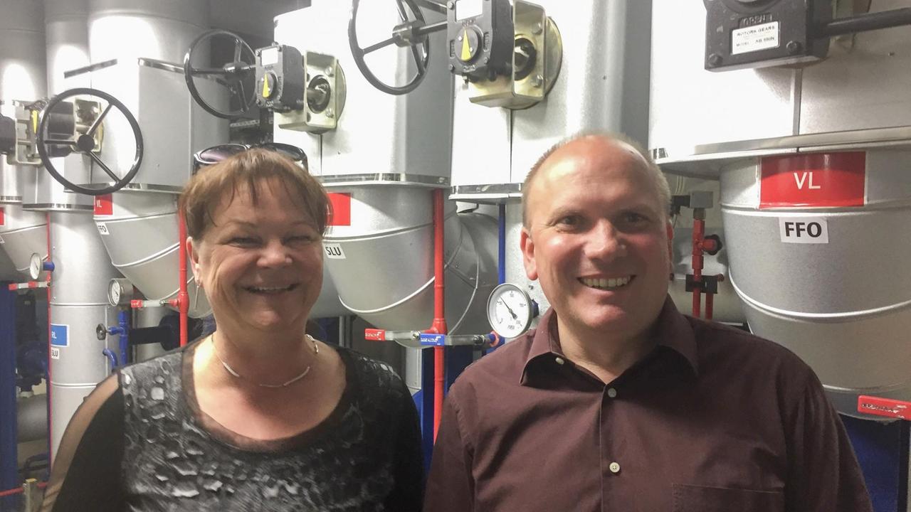 Antje Bodsch und Harald Wolf von den Stadtwerken Frankfurt (Oder) blicken, in der Wärmeübertragungsstation stehend, in die Kamera und lachen. Antje Bodsch und Harald Wolf von den Stadtwerken Frankfurt (Oder) blicken, in der Wärmeübertragungsstation stehend, in die Kamera und lachen.