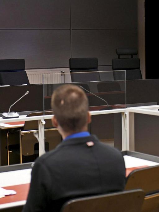 Das Foto zeigt einen abgedunkelten Gerichtssaal mit einem Bildschirm, auf dem ein Tatverdächtiger per Videoübertragung an der Gerichtssitzung teilnimmt.