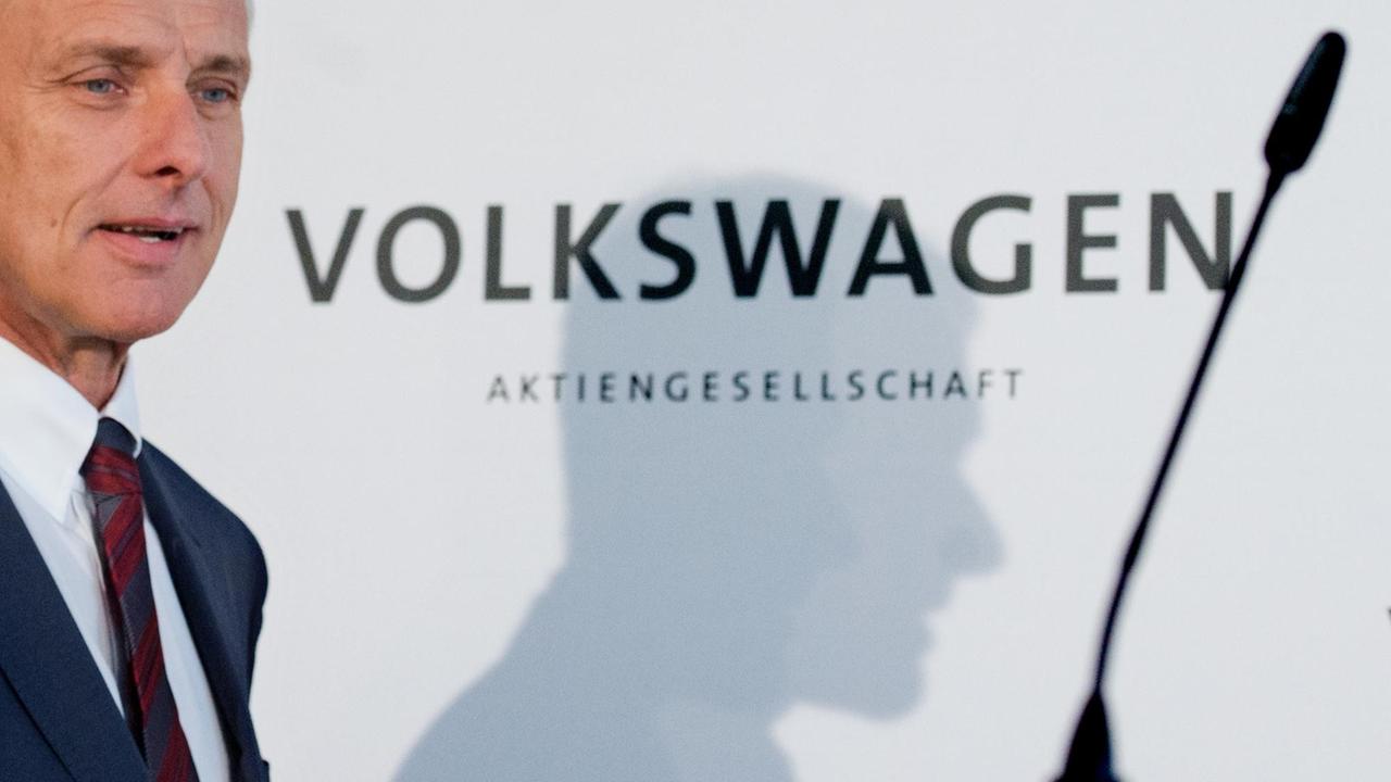 Müller auf dem Weg zu einem Mikrofon bei einer Pressekonferenz. An der weißem Wand hinter ihm steht "Volkswagen Aktiengesellschaft". Müller auf dem Weg zu einem Mikrofon bei einer Pressekonferenz. An der weißem Wand hinter ihm steht "Volkswagen Aktiengesellschaft".