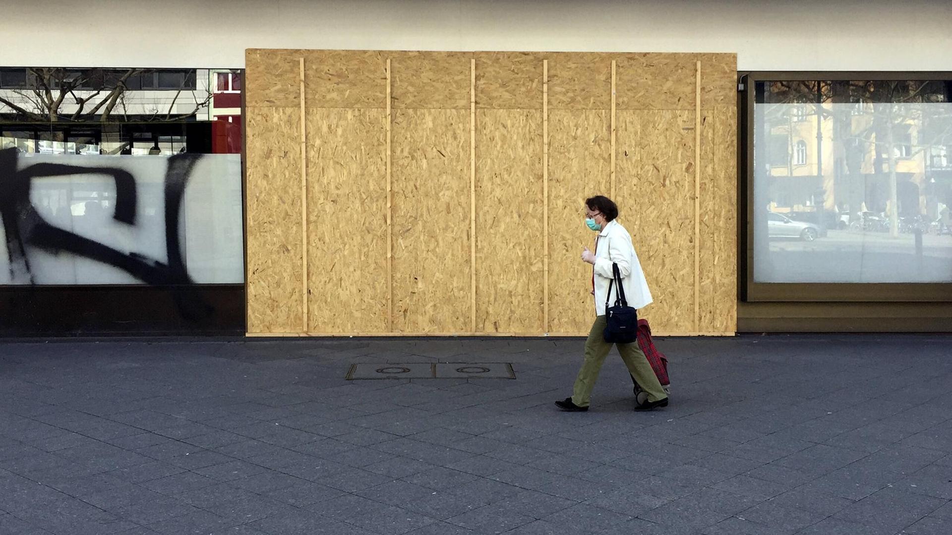 Mit Holzplatten verrammeltes Geschäft auf dem Kurfürstendamm in Berlin, während eine Passantin mit Corona-Schutzmaske vorbeiläuft.