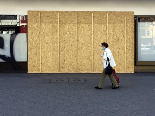 Mit Holzplatten verrammeltes Geschäft auf dem Kurfürstendamm in Berlin, während eine Passantin mit Corona-Schutzmaske vorbeiläuft.