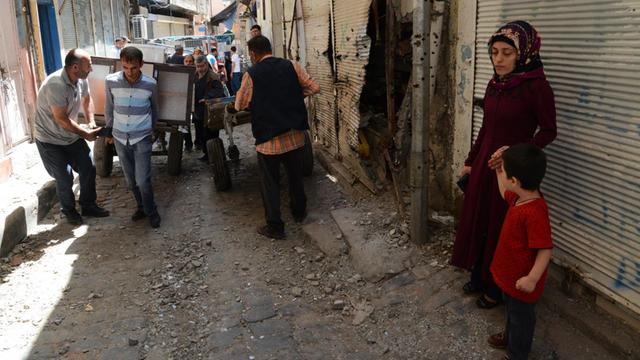 Eine Frau und ein Kind schauen in der hnistorischen Altstadt von Diyarbakir auf eine Gruppe von Männern bei Aufräumarbeiten.