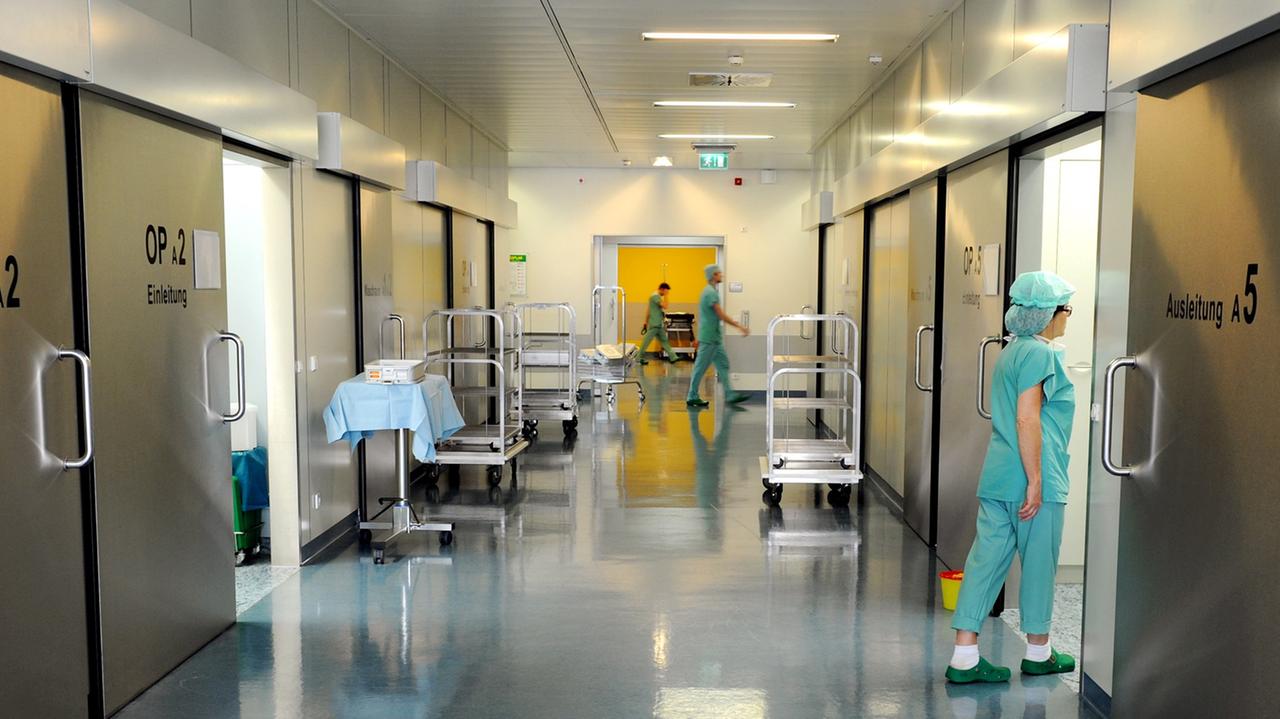 In einem Krankenhaus laufen Mitarbeiter über den Flur. In einem Krankenhaus laufen Mitarbeiter über den Flur.