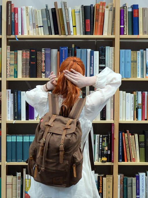 Eine Besucherin steht auf der Leipziger Buchmesse 2017 vor einem Regal mit Büchern.