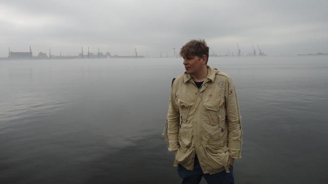 Komponist Sergej Newski steht vor einem düsteren Seehafenpanorama