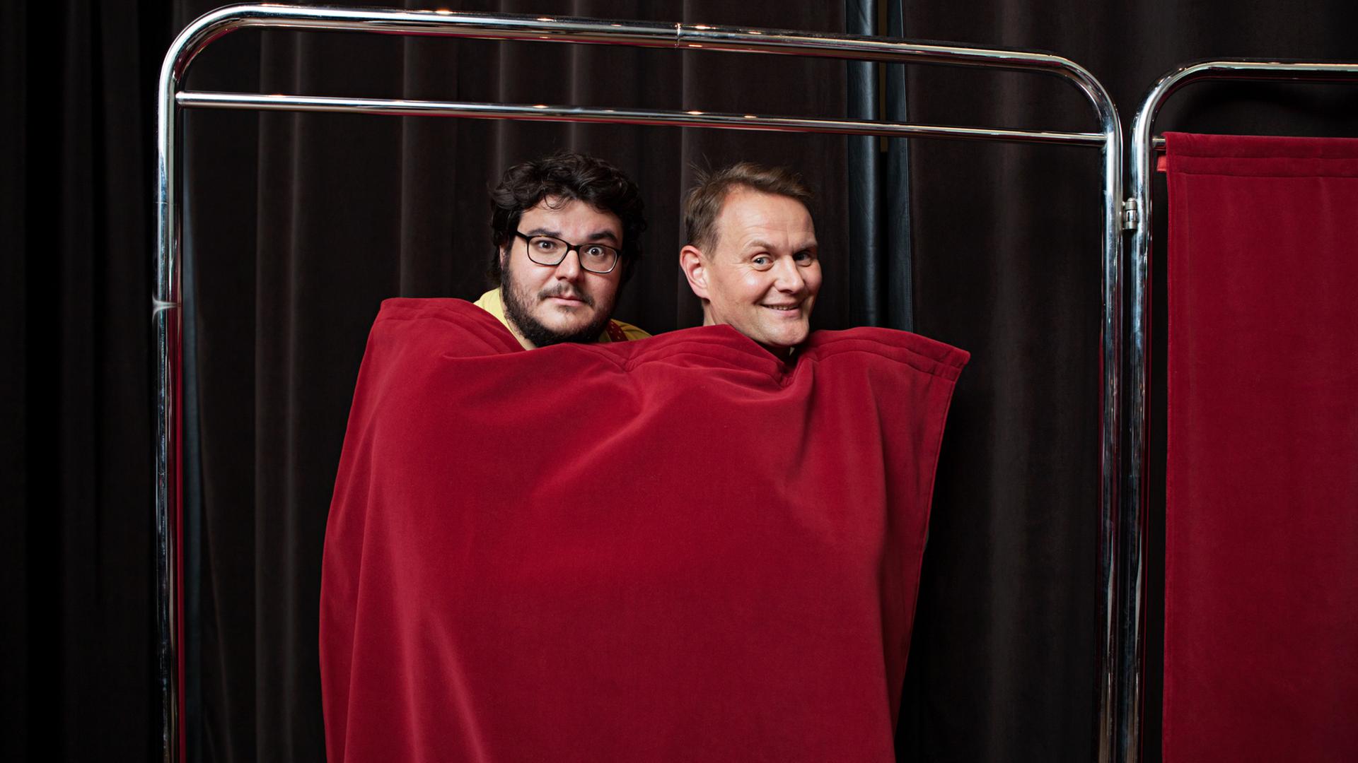 Das Bild zeigt Axel Ranisch und Devid Striesow, die sich zusammen in einen roten Vorhang eingewickelt haben. Das Bild zeigt Axel Ranisch und Devid Striesow, die sich zusammen in einen roten Vorhang eingewickelt haben.