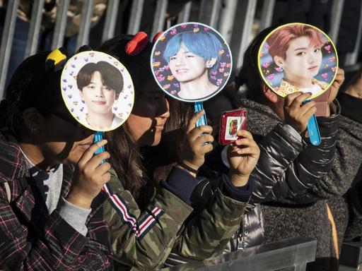 Fans warten auf den Auftritt der K-Pop Gruppe BTS im Central Park, New York und schützen sich mit Fächern, auf den die einzelnen Bandmitglieder abgebildet sind, vor de Sonne.