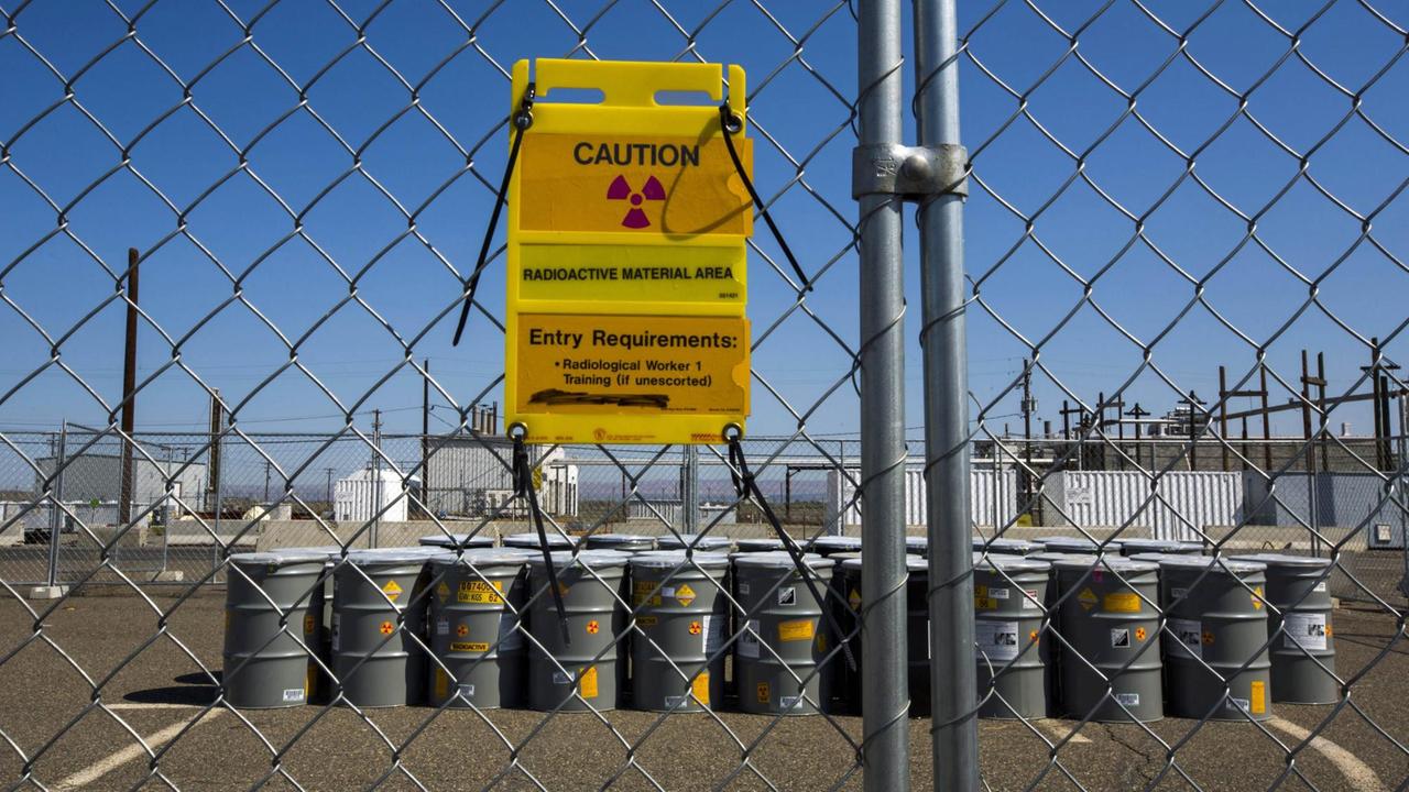 Tanks in der Atommülldeponie Hanford Site hinter einem Zaun, davor ein Schild, das vor radioaktiver Strahlung warnt.