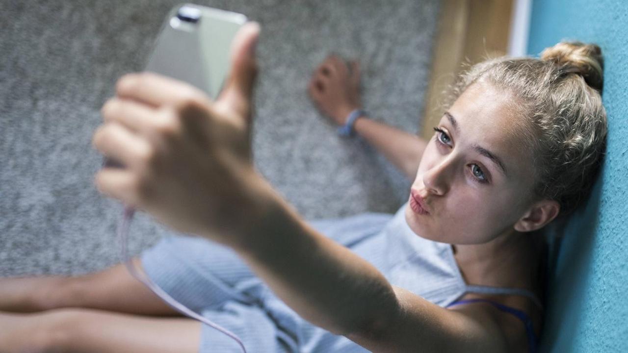 Ein Mädchen sitzt in seinem Zimmer auf dem Boden und macht Selfies. Ein Mädchen sitzt in seinem Zimmer auf dem Boden und macht Selfies.
