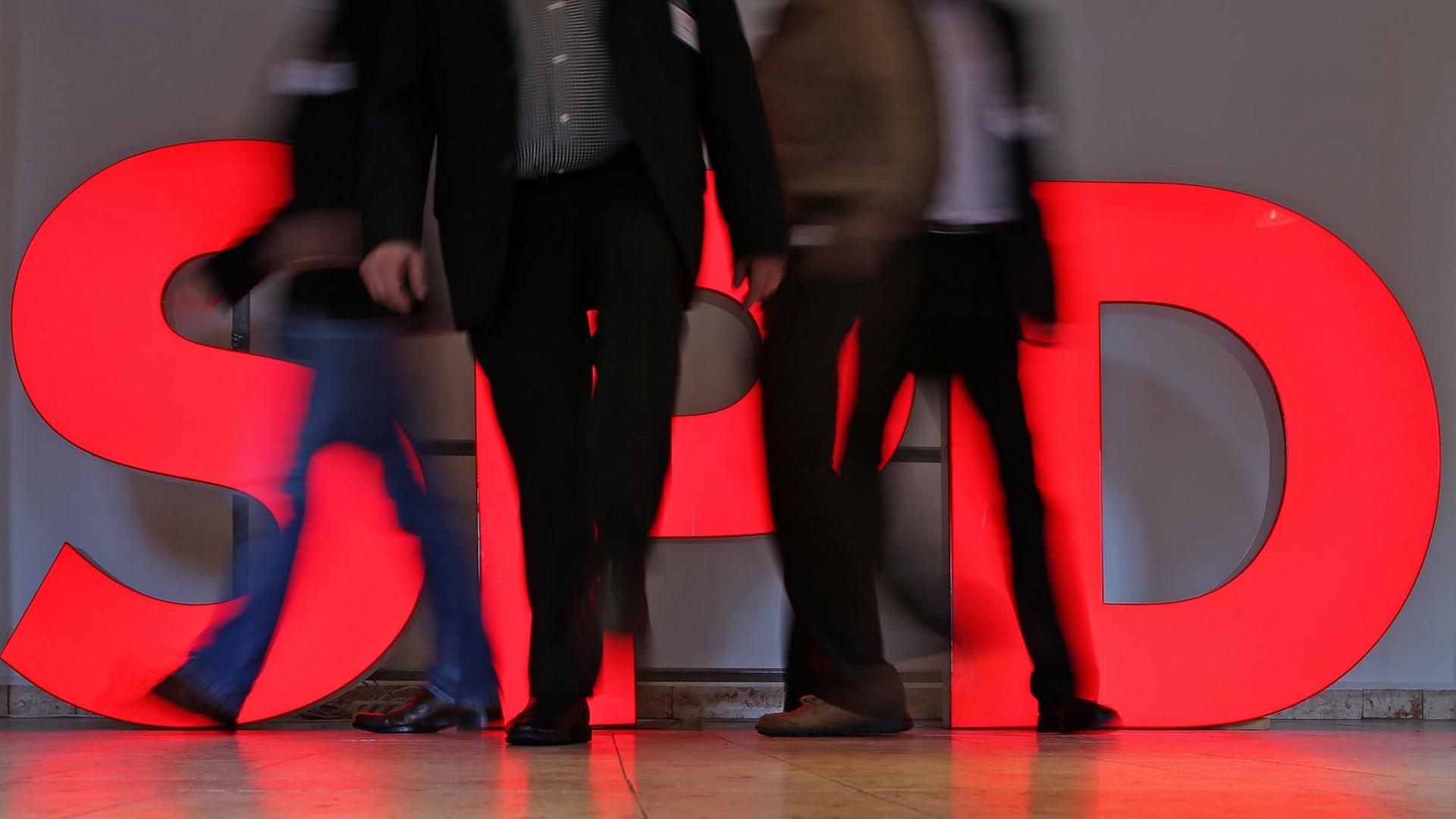 Parteimitglieder der SPD gehen an einem beleuchteten Parteilogo vorbei
