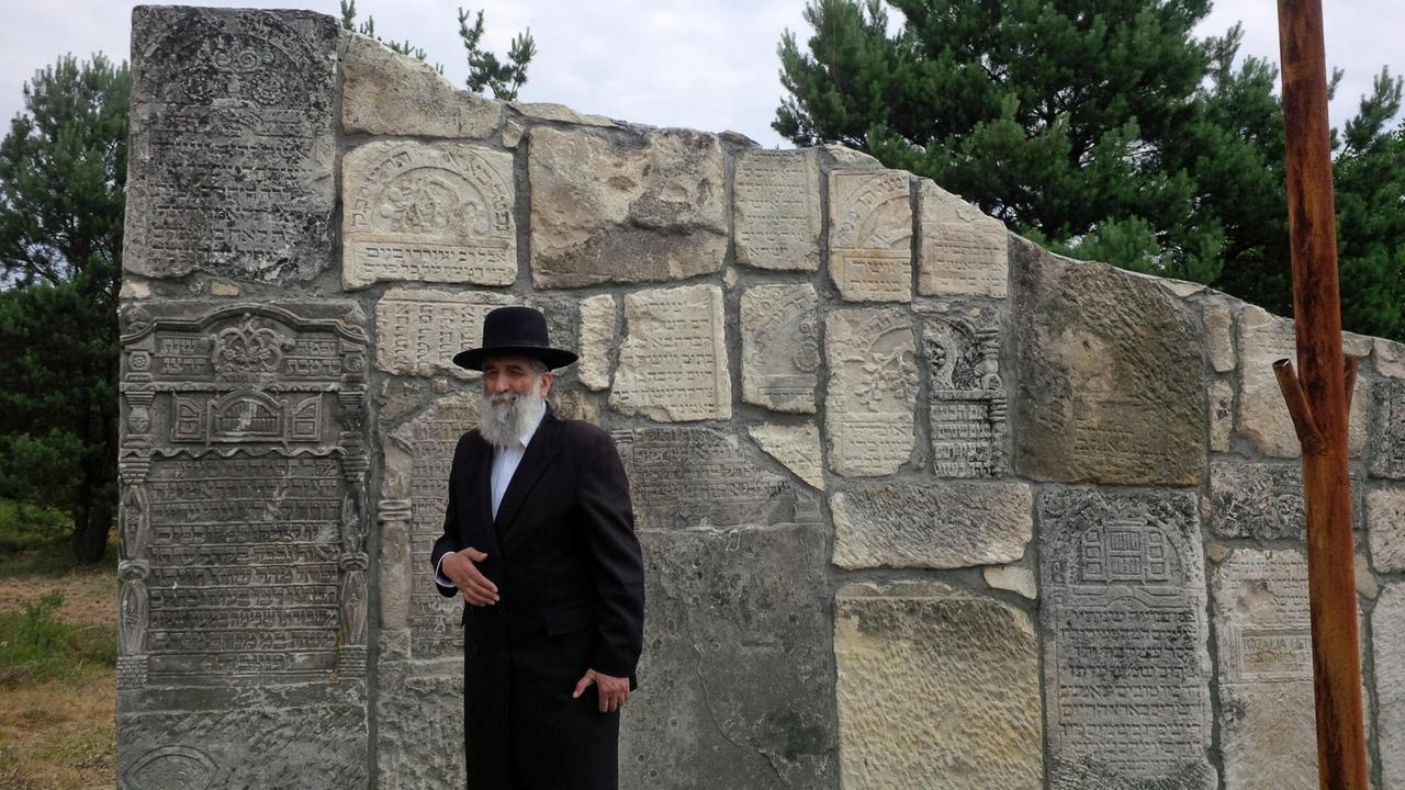 Meylach Sheykhet, jüdischer Publizist aus Lemberg bei der Eröffnung der Gedenkstätte Rava-Ruska steht vor einer Mauer mit einer Inschrift