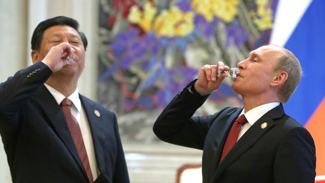 Chinas Präsident Xi Jinping und Russlands Präsident Wladimir Putin stehen nebeneinander und trinken aus jeweils einem kleinen Glas.