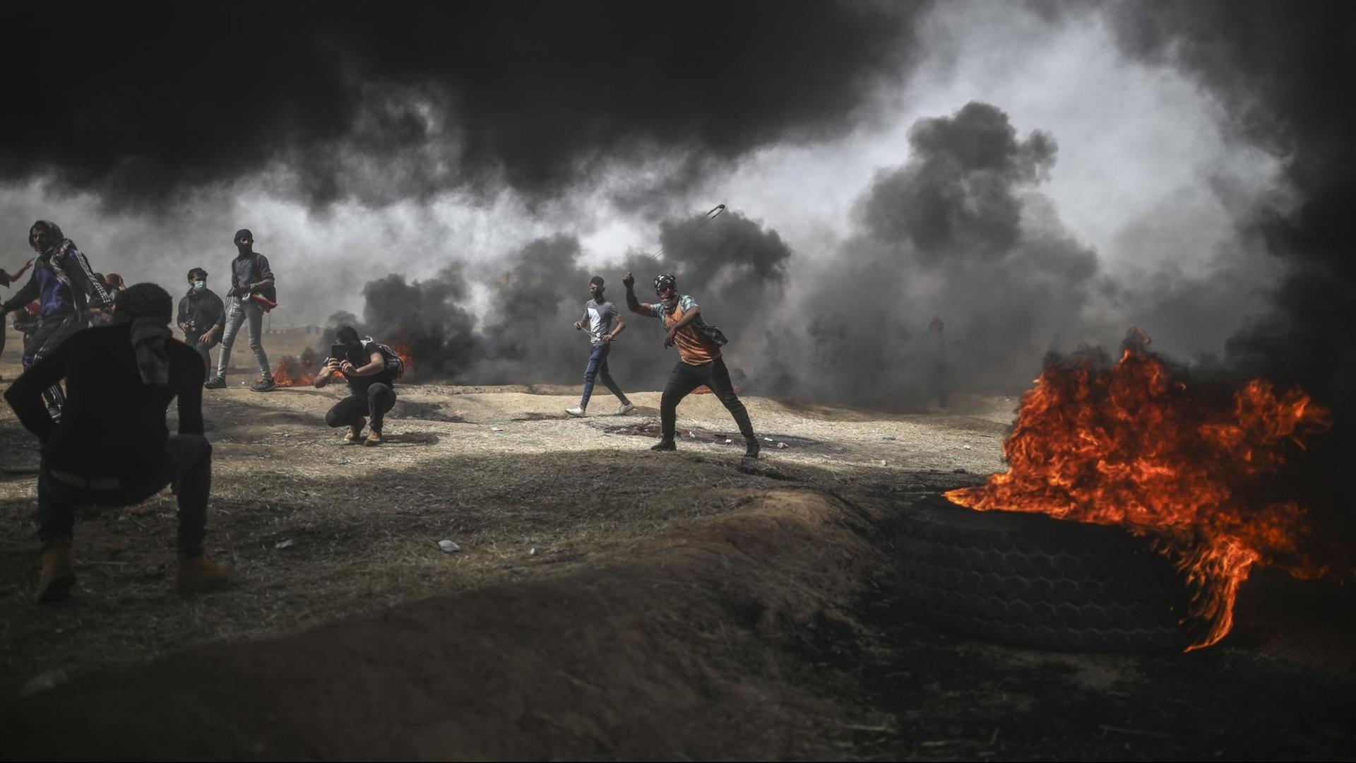 Palästinensische Autonomiegebiete, Gaza: Ein palästinensischer Mann zielt während eines Protests mit einer Steinschleuder auf israelische Soldaten.