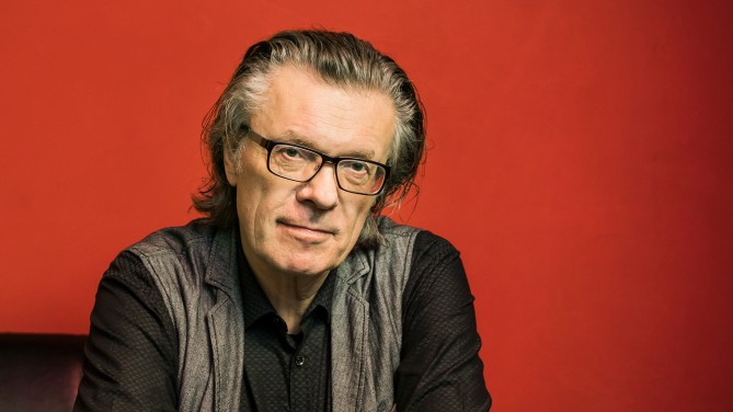 Porträt des Kulturphilosophen Ralf Konersmann, mit zurückgekämmtem Haar und schwarz gerahmter Brille, in schwarzem Pullover und grauer Weste, vor einer ochsenblutroten Wand Porträt des Kulturphilosophen Ralf Konersmann, mit zurückgekämmtem Haar und schwarz gerahmter Brille, in schwarzem Pullover und grauer Weste, vor einer ochsenblutroten Wand