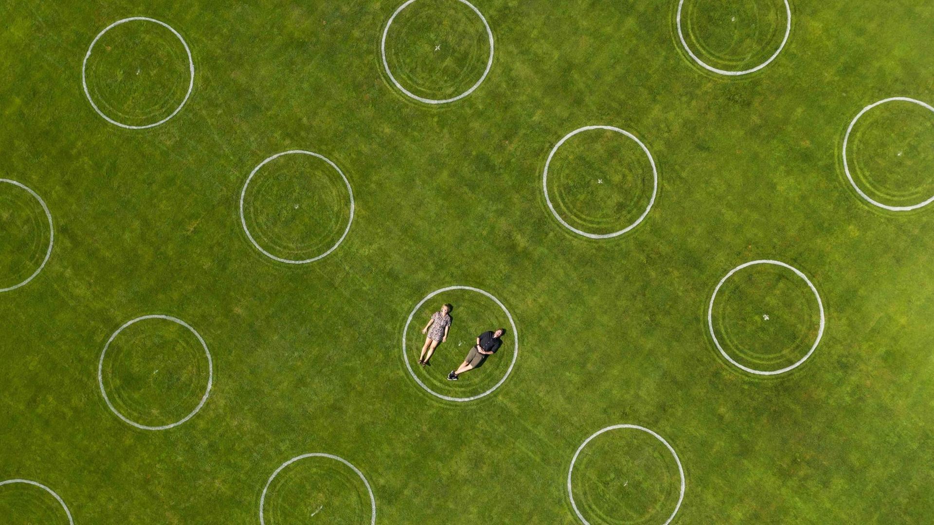 Luftaufnahme eines Stadions mit eingezeichneten Kreidekreisen für die Abstandseinhaltung bei einer Veranstaltung im Jahnstadion, Göttingen. In einem der Kreise liegt ein Paar nebeneinander.