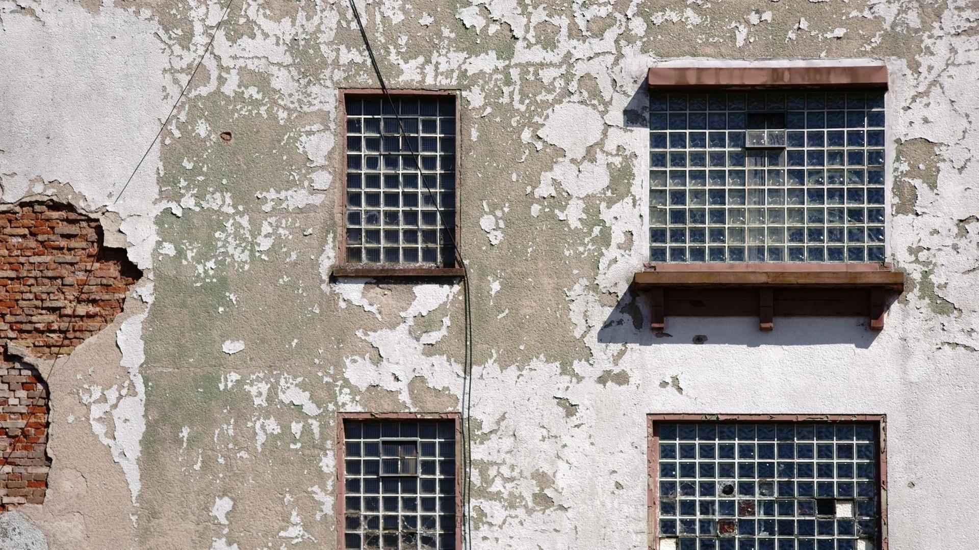Fassade mit sich lösendem Putz und teilweise kaputten Glasfliesenfenstern. Fassade mit sich lösendem Putz und teilweise kaputten Glasfliesenfenstern.