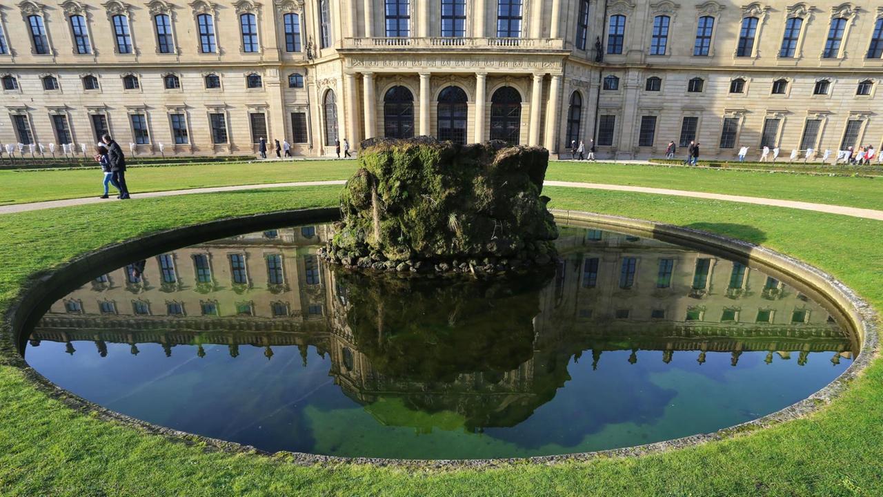Spaziergänger gehen am 27.12.2015 im Hofgarten der Residenz in Würzburg (Bayern) hinter einem Brunnen entlang, in dem sich Teile der Residenz spiegeln. Spaziergänger gehen am 27.12.2015 im Hofgarten der Residenz in Würzburg (Bayern) hinter einem Brunnen entlang, in dem sich Teile der Residenz spiegeln.