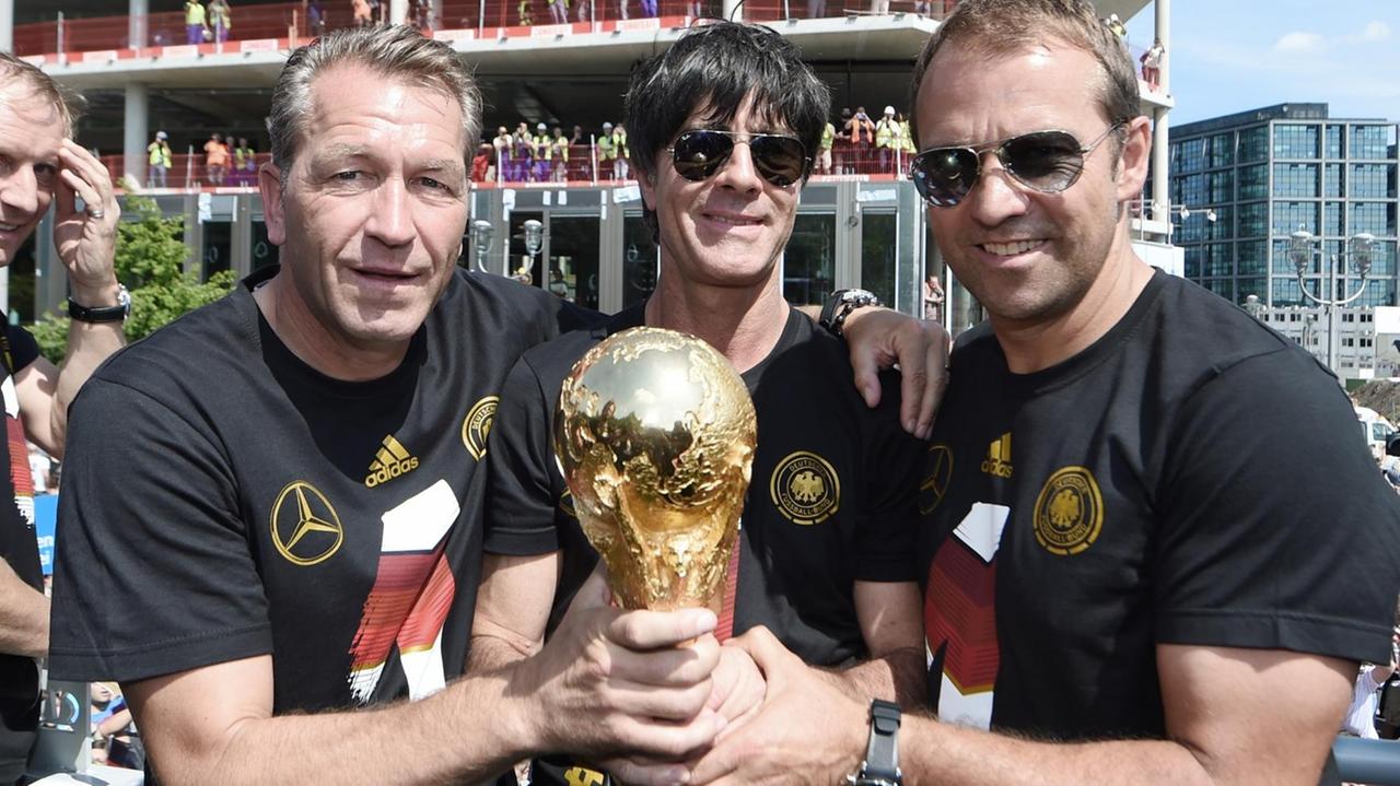 2014: Torwarttrainer Andreas Koepke, Bundestrainer Joachim Löw und der damalige Assistenztrainer Hansi Flick fassen gemeinsam den Weltermeisterschaftspokal an.