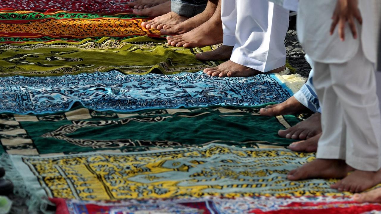 Bunte Gebetsteppiche und Beine von Männern, die sich zum Gebet aufgestellt haben. Bunte Gebetsteppiche und Beine von Männern, die sich zum Gebet aufgestellt haben.