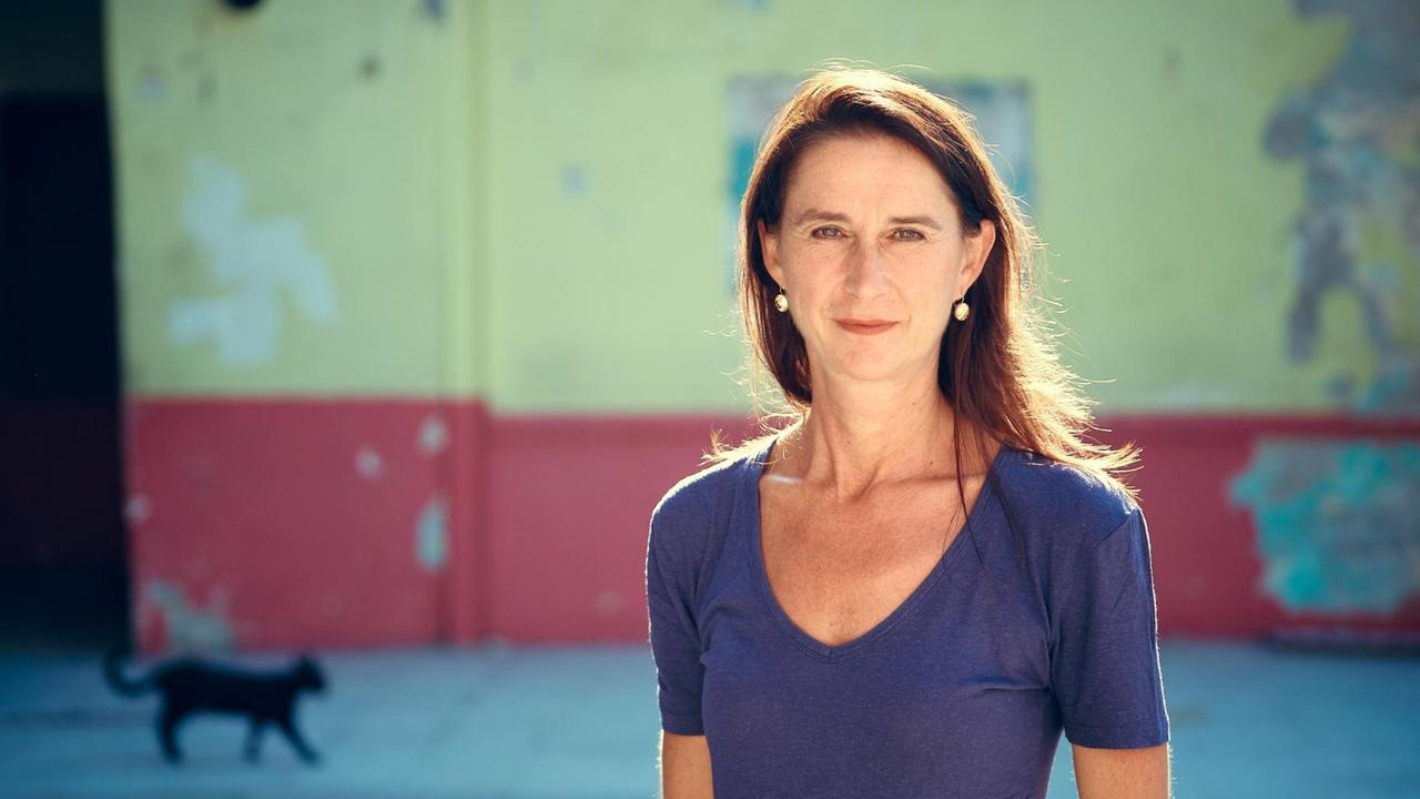 Eine Frau mit langen dunkelbrauen Haaren und dunkelblauem kurzärmligen T-Shirt steht in der Sonne. Im Hintergrund eine schwarze Katze. Eine Frau mit langen dunkelbrauen Haaren und dunkelblauem kurzärmligen T-Shirt steht in der Sonne. Im Hintergrund eine schwarze Katze.