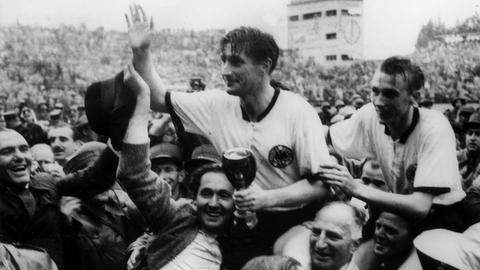 Die deutschen Fußballspieler Fritz Walter (M, mit dem Pokal in den Händen) und Horst Eckel (r) werden am 4.7.1954 von Fans frenetisch gefeiert und auf den Schultern durch das Stadion getragen.