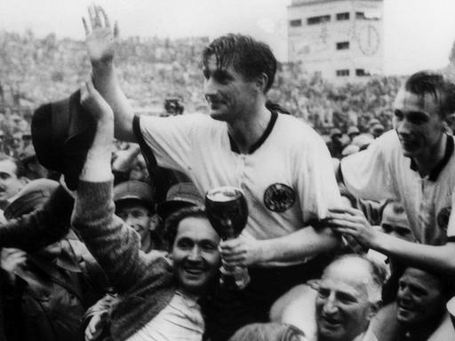 Die deutschen Fußballspieler Fritz Walter (M, mit dem Pokal in den Händen) und Horst Eckel (r) werden am 4.7.1954 von Fans frenetisch gefeiert und auf den Schultern durch das Stadion getragen.