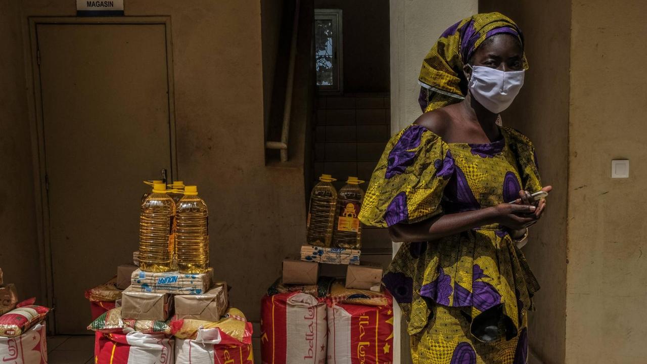 Eine Frau mit Maske vor Lebensmittelrationen, die an die Bevölkerungs im Senegal verteilt werden soll, die aufgrund von Coronamaßnahmen ihr Einkommen verloren haben.63 Eine Frau mit Maske vor Lebensmittelrationen, die an die Bevölkerungs im Senegal verteilt werden soll, die aufgrund von Coronamaßnahmen ihr Einkommen verloren haben.63