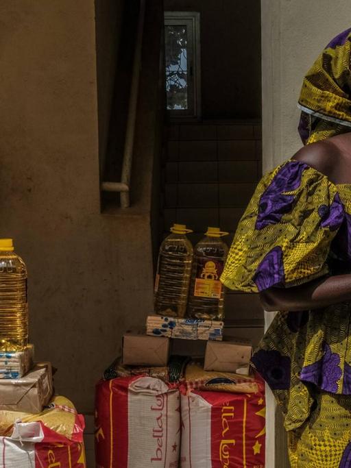 Eine Frau mit Maske vor Lebensmittelrationen, die an die Bevölkerungs im Senegal verteilt werden soll, die aufgrund von Coronamaßnahmen ihr Einkommen verloren haben.63