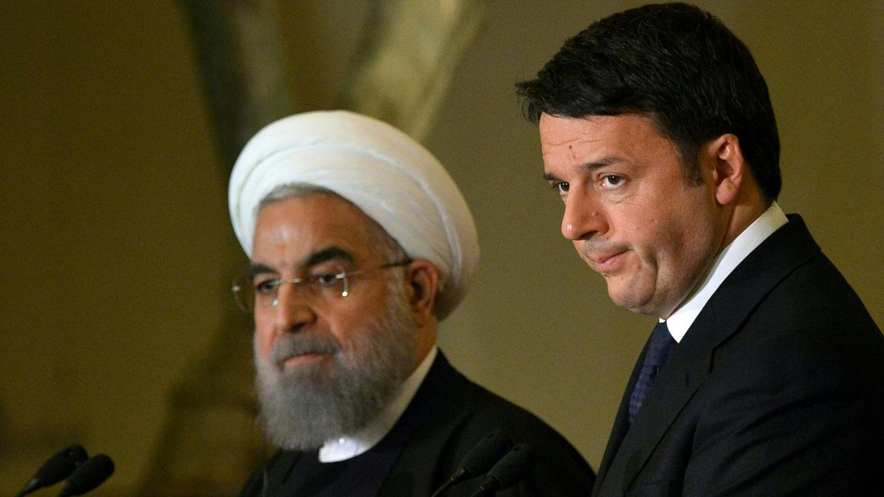 Man sieht Rohani und Renzi mit ernsten Blicken vor vier Mikrofonen. Im Hintergrund eine olivgrüne Wand.