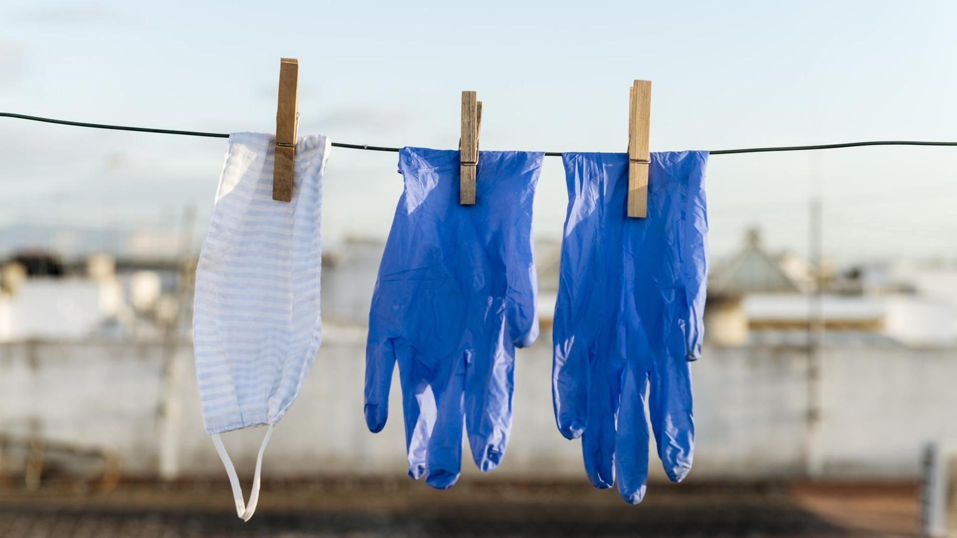 Gesichtsmaske und Handschuhe hängen über der Wäscheleine.