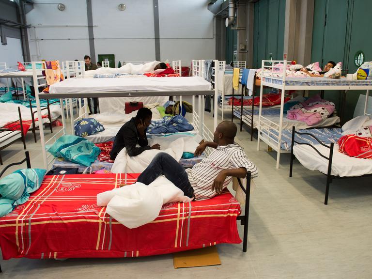 Flüchtlinge aus verschiedenen Ländern sitzen und liegen im Erstaufnahmelager der Bayernkaserne in München (Bayern) in den Betten ihrer Unterkunft, die in einer ehemaligen Bundeswehr-LKW-Garage eingerichtet wurde.