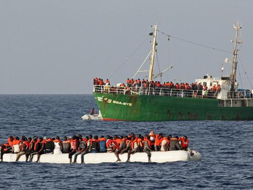 Ein mit Flüchtlingen besetztes Schlauchboot. Im Hintergrund das Seenotrettungsschiff "Sea Eye"