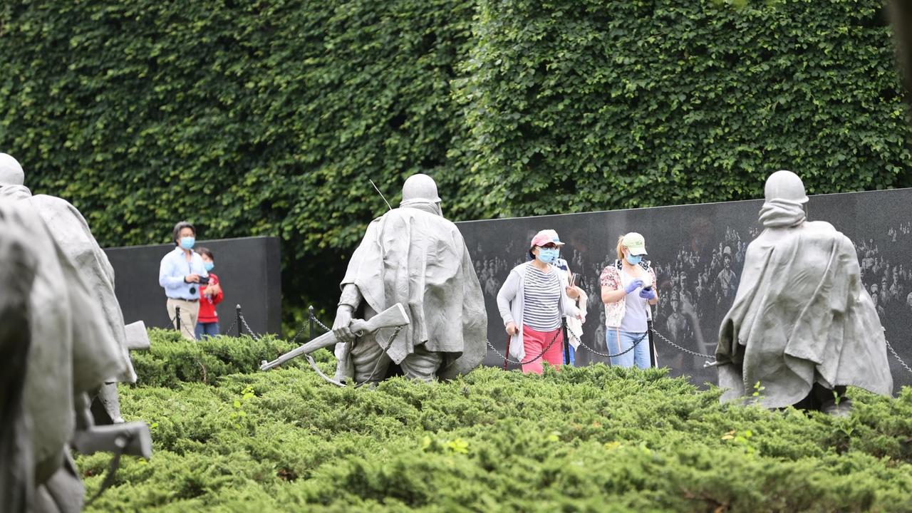 Mit Mundschutz gehen Menschen am Statuen vo Vietnamveteranen in der National Mall vorbei. 